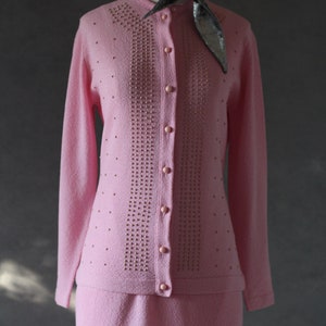 Peut inclure: Un ensemble jupe et cardigan en tricot rose avec un motif perl&eacute;. Le cardigan a une fermeture boutonn&eacute;e et des manches longues. La jupe est mi-longue.