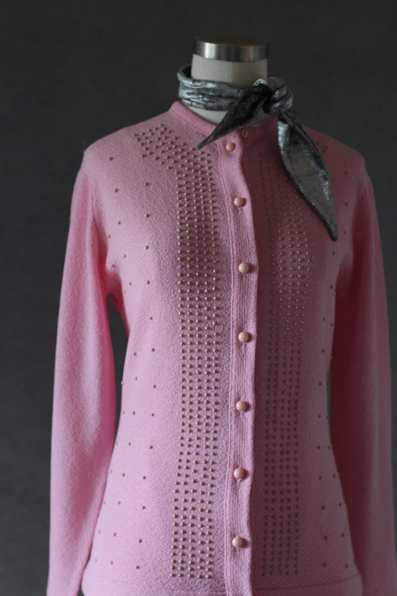 Peut inclure: Un cardigan rose avec un devant boutonn&eacute; et un motif perl&eacute;. Le cardigan est en tricot textur&eacute; et orn&eacute; de petites perles rondes dispos&eacute;es en motif vertical.