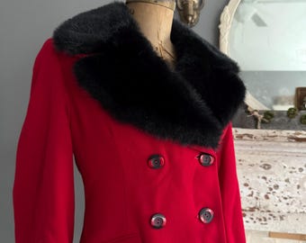Puede incluir: Un abrigo rojo vintage de doble botonadura con cuello de piel sintética negra. El abrigo presenta seis botones oscuros y un corte entallado, exhibido en un maniquí vintage. El color vibrante y el diseño clásico sugieren una estética retro.