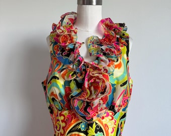 May include: A sleeveless dress featuring a vibrant, multi-colored paisley pattern in shades of bright pink, lime green, orange, blue, and black. The garment includes a prominent, ruffled collar detail that cascades down the center of the bodice.