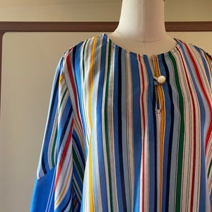 Peut inclure: Une chemise à rayures bleues et blanches avec des rayures colorées. La chemise a un col rond et une fermeture à bouton.