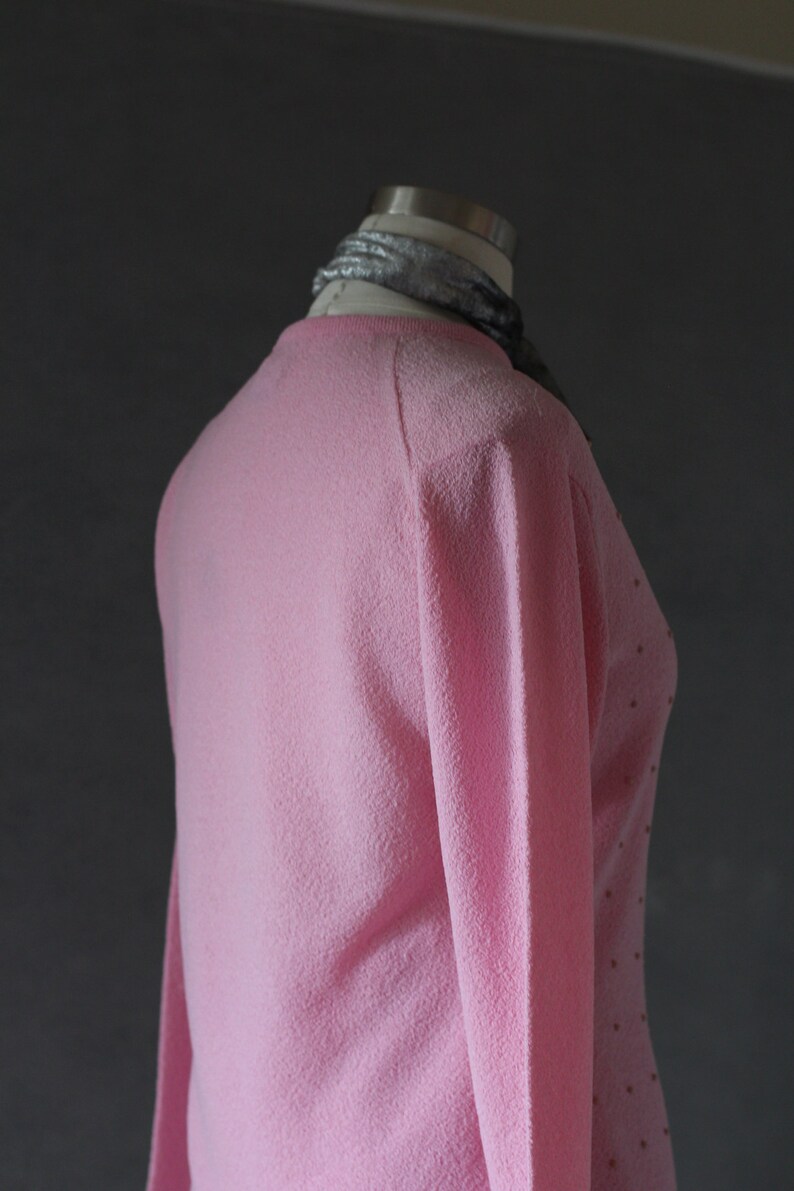 Peut inclure: Un pull rose avec un motif de pois subtils. Le pull est fait d'un mat&eacute;riau doux et duveteux et a des manches longues.