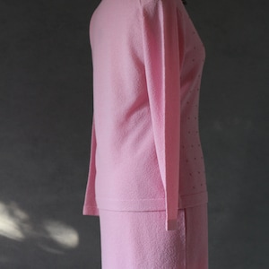 Peut inclure: Un ensemble de jupe et de pull rose. Le pull a des manches longues et un col rond. La jupe est mi-longue et a une silhouette droite.
