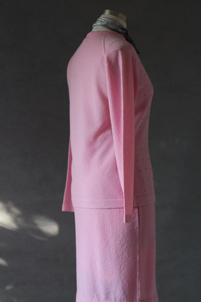 Peut inclure: Un ensemble de jupe et de pull rose. Le pull a des manches longues et un col rond. La jupe est mi-longue et a une silhouette droite.