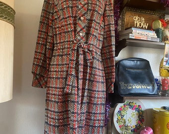 May include: A long-sleeved dress with a plaid pattern in shades of red, black, and white. The dress has a collared neckline, a button-up front, and a tie belt at the waist.