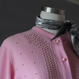Peut inclure: Un cardigan rose avec un motif perl&eacute; et une &eacute;charpe argent&eacute;e nou&eacute;e autour du cou.