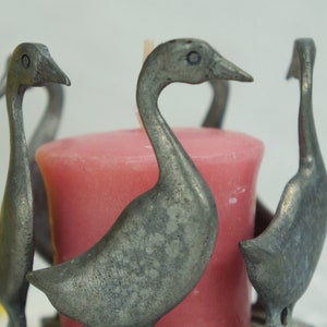 May include: A silver candle holder shaped like four geese with a pink candle in the center.