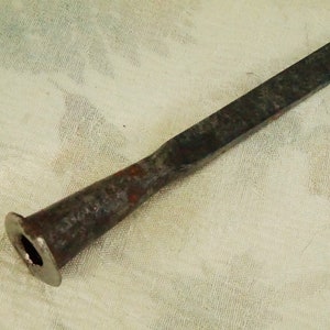 Puede incluir: Un cincel de metal oxidado con un mango acampanado y redondeado. El cincel mide aproximadamente 25 cm de largo.