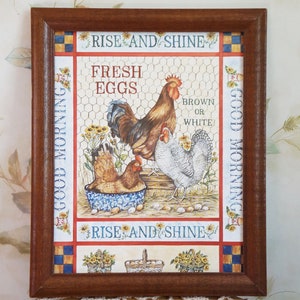 Könnte beinhalten: Ein gerahmter Druck mit einem Hahn, Hühnern und Eiern. Der Druck hat ein rot-weiß-blaues Farbschema und sagt "Good Morning" und "Rise and Shine" an den Seiten. Der Text sagt auch "Fresh Eggs" und "Brown or White".