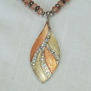 May include: A silver pendant necklace with a teardrop-shaped charm. The charm is decorated with a multi-coloured enamel design and clear rhinestones.
