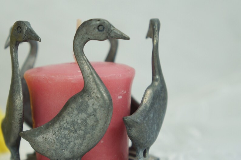 May include: A silver candle holder shaped like four geese with a pink candle in the center.