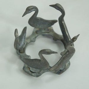 May include: A silver metal birdcage shaped candle holder with five bird figurines. The birds are arranged in a circle around the center of the cage.
