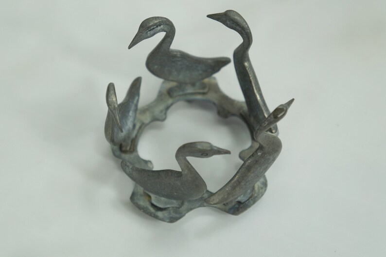 May include: A silver metal birdcage shaped candle holder with five bird figurines. The birds are arranged in a circle around the center of the cage.