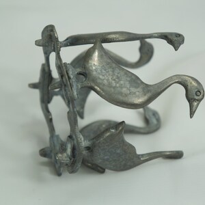 May include: A silver metal sculpture of four geese, each with a long neck and a curved beak. The geese are arranged in a circle, with their necks intertwined. The sculpture is a decorative piece that would look great on a shelf or table.