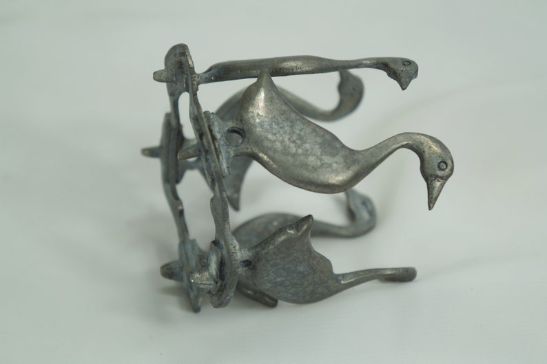 May include: A silver metal sculpture of four geese, each with a long neck and a curved beak. The geese are arranged in a circle, with their necks intertwined. The sculpture is a decorative piece that would look great on a shelf or table.