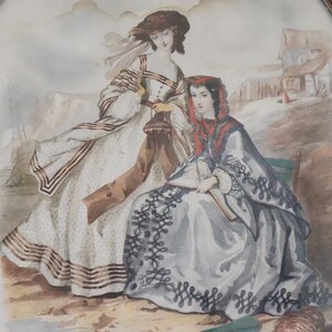 May include: Two women in vintage clothing are depicted in an oval-shaped painting. The woman on the left wears a white dress with brown and black stripes, a brown shawl, and a white hat. The woman on the right wears a gray dress with black lace trim, a red shawl, and a black hat. The painting is set against a backdrop of a small village.