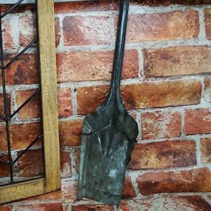 May include: A black metal scoop with a wooden handle. The scoop is sitting on a brick wall background.