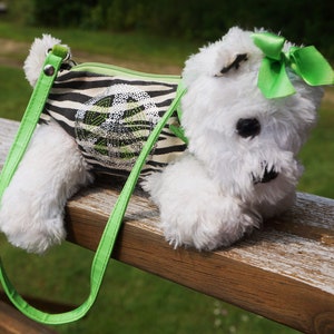May include: A white plush toy shaped like a dog with a green and white striped fabric bag attached. The bag has a green strap and a green bow on the dog's head.