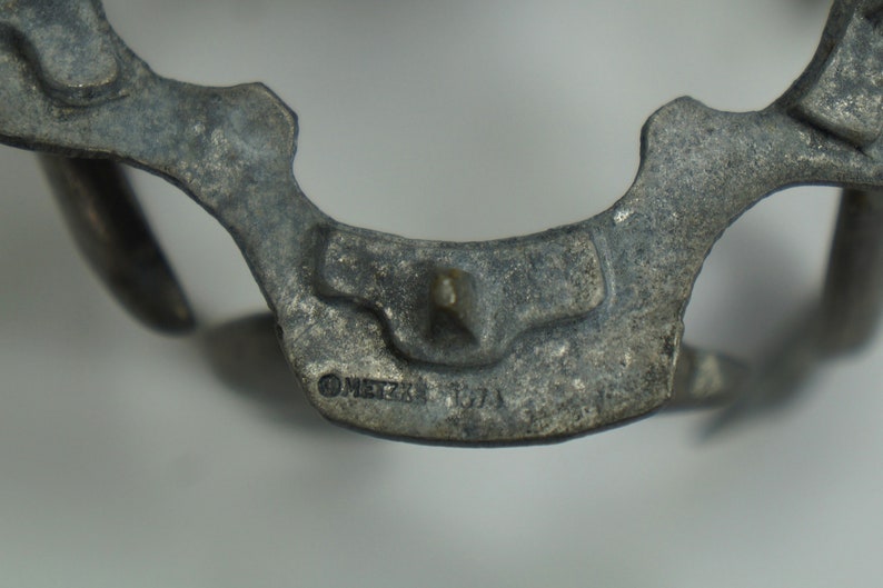 May include: Close-up of a silver-toned metal object with a detailed design. The object has a pointed tip and a circular inscription that reads "METZKE 170A".