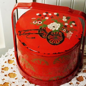 May include: Red lacquered box with a handle, decorated with gold floral designs and a cart with wheels. The box has a worn, vintage look.