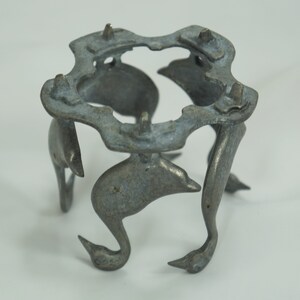 May include: A silver metal stand with a circular top and five legs shaped like stylized birds. The stand is made of a lightweight metal and has a slightly distressed finish.