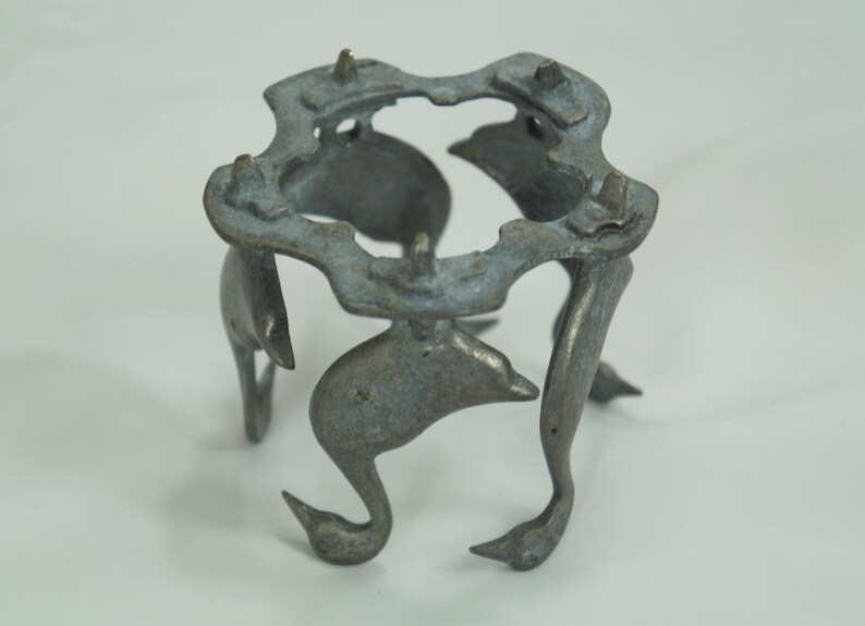 May include: A silver metal stand with a circular top and five legs shaped like stylized birds. The stand is made of a lightweight metal and has a slightly distressed finish.