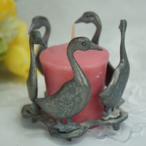May include: A silver candle holder shaped like a group of geese surrounding a pink votive candle.