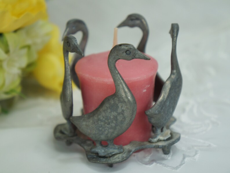 May include: A silver candle holder shaped like a group of geese surrounding a pink votive candle.