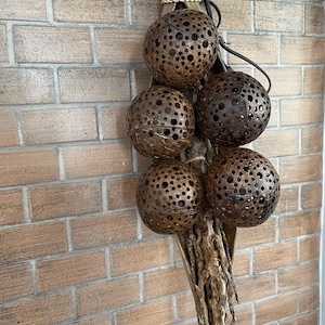 May include: A cluster of six brown coconut shell light fixtures hang from a woven rope and a natural branch. The fixtures are attached to a black wire and have a pattern of small holes throughout the shell.