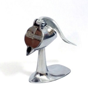 May include: A silver metal citrus juicer with a lever and a spout. The juicer is designed to be placed on a countertop.