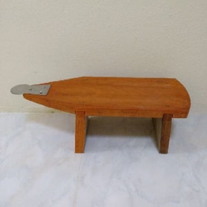 May include: A wooden stool with a flat top and a metal footrest. The stool is made of light brown wood and has a simple design.