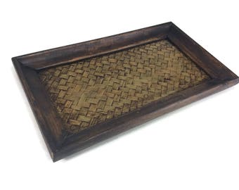 Può includere: Un vassoio rettangolare in legno con un inserto in bambù intrecciato. Il vassoio è marrone scuro e il bambù è di colore marrone chiaro.
