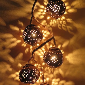 May include: A decorative light fixture made from coconuts with intricate cutouts. The coconuts are strung together with rope and lit from within, casting warm, patterned light on the wall.
