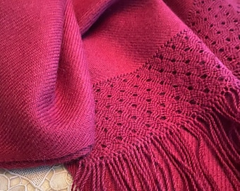 May include: A deep burgundy shawl with a delicate lace pattern and long fringe. The shawl is made of a soft, luxurious fabric.