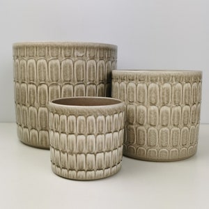 May include: Three ceramic plant pots in different sizes, all with a textured, light brown finish. The pots have a unique, geometric pattern.
