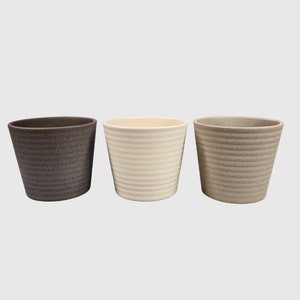 May include: Three ceramic plant pots in different colours: brown, white and beige. The pots have a textured, ribbed design.
