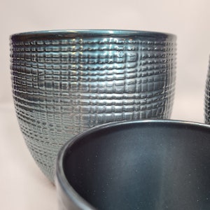 May include: Two teal ceramic planters with a textured, woven design. The planters are round and have a wide opening.