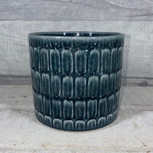 May include: A dark blue ceramic planter with a textured, geometric pattern. The planter is cylindrical in shape and has a smooth, glazed finish.
