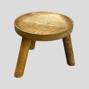 May include: A wooden stool with a round top and three legs. The stool is made of natural wood and has a light brown colour.