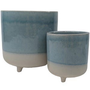 May include: Two blue and white ceramic planters, each with three legs. The larger planter is taller and wider than the smaller planter.