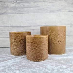 May include: Three brown ceramic planters with a textured surface. The planters are different sizes and are arranged in a row from largest to smallest.