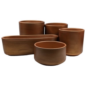 May include: Set of five gold-coloured ceramic planters, including a round planter, an oval planter, and three cylindrical planters.
