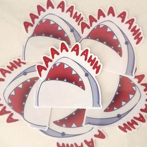 Op de afbeelding: Een set van vijf witte haaien stickers met rode open monden en het woord "AAAAAH" in het rood rond de haai.