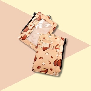 May include: Two beige card holders with a brown and white pattern of bread and pastries. The card holder on the left has a clear plastic window. Both card holders have a zipper closure.