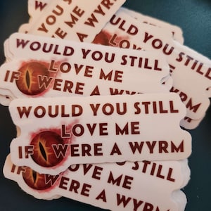 Op de afbeelding: Een stapel witte stickers met rode tekst en een rode oogafbeelding. De tekst op de stickers luidt "Would you still love me if I were a wyrm?"