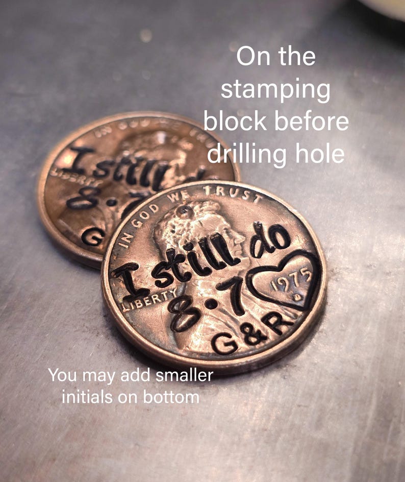 May include: Two copper-colored United States one-cent coins featuring stamped black text. The coins are engraved with the words I still do, the date 8.7, the year 1975 inside a heart shape, and the initials G&R, with Liberty and In God We Trust.