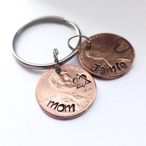 May include: A silver key chain with two copper pennies attached. One penny has the word "Mom" engraved on it and the other has the word "Jamie" engraved on it.
