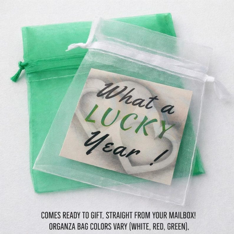 May include: A sheer white organza drawstring bag containing a square card with the text What a LUCKY Year! printed in black and green, layered over a solid green organza drawstring bag. The bags feature a ribbon closure at the top.