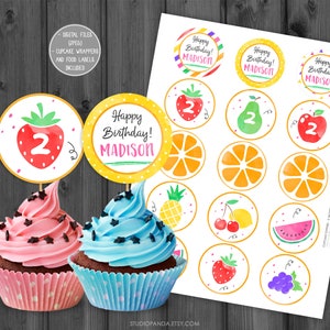 May include: Printable cupcake toppers featuring a watercolour fruit theme. The toppers include a variety of fruits such as strawberries, pears, oranges, pineapples, cherries, watermelons and grapes. The toppers are designed for a 2nd birthday party and include the name "Madison" and the number "2".
