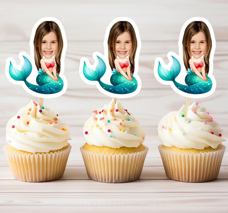 May include: Three cupcakes decorated with colorful sprinkles and topped with mermaid-themed cake toppers. Each topper features a mermaid with a turquoise tail and a girl's face.
